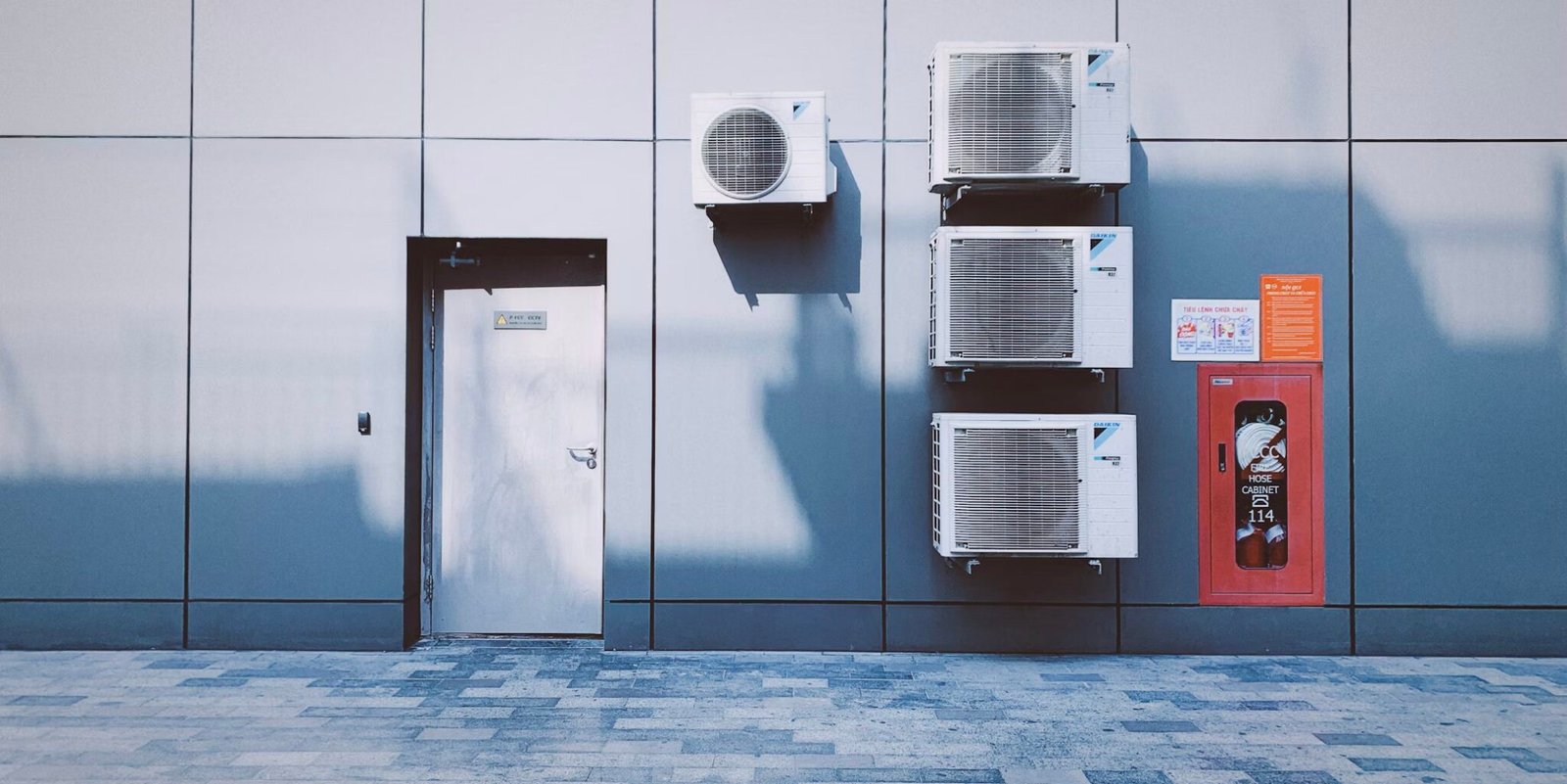 Row of outdoor air conditioning condenser units installed on the exterior wall of a commercial building.