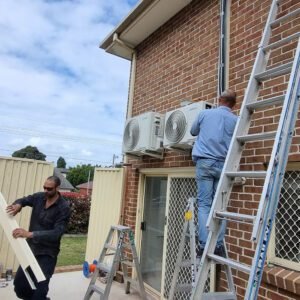 Technicians installing a reverse cycle air conditioning system on the exterior wall of a house.